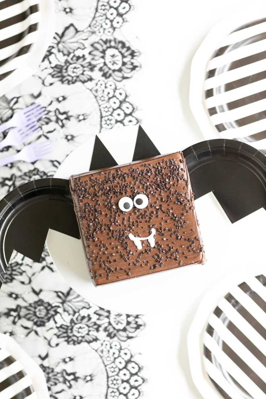 Dark chocolate cake shaped like a bat with orange frosting wings on a black serving board
